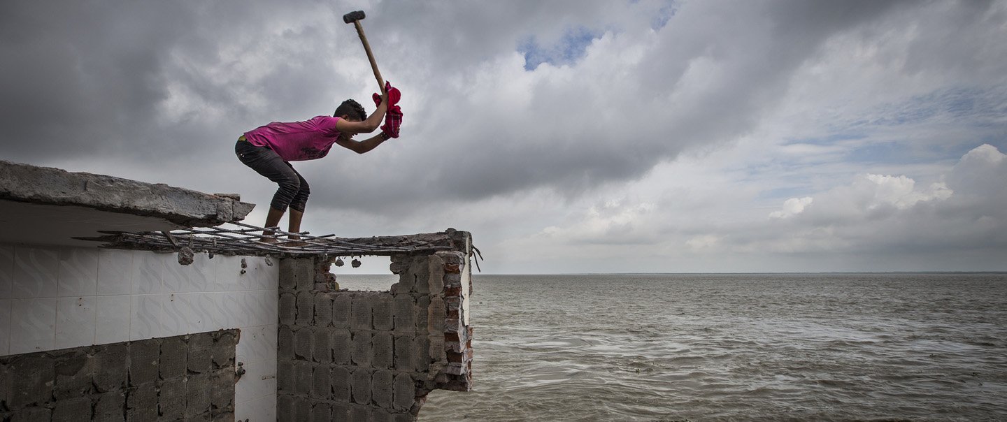Frau zertrümmert mit dem Hammer die Mauer eines Hauses am Meer