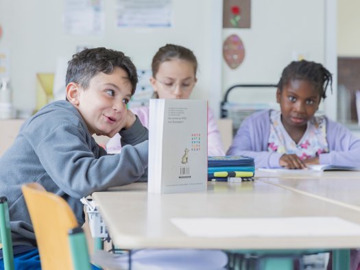 Drei Grundschulkinder sitzen an einem Tisch und lesen