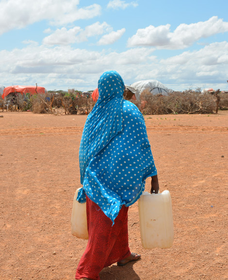 Eine Frau trägt Wasserkanister in einer Siedlung für Binnenvertriebene in Gumays, Somalia.