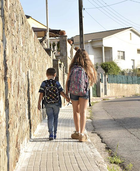 Zwei Schüler halten einander an den Händen und laufen eine Straße entlang