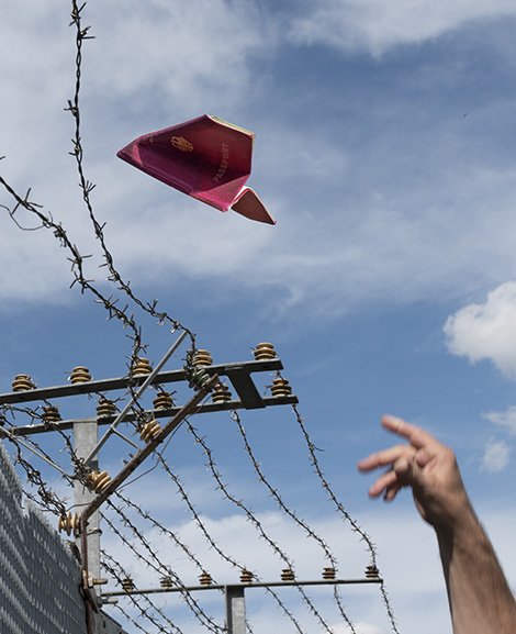 Ein Papierflieger, der über einen Grenzzaun fliegt.