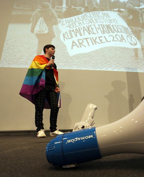 Jugendlicher auf der Bühne mit Regenbogenfahne und Megaphon