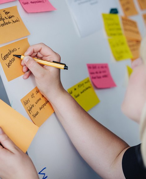 Eine Frau schreibt auf einem Board mit mehreren bunten Post-Its