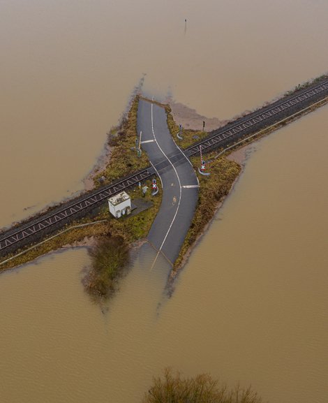 Das Bild zeigt ein überflutetes Gebiet von oben. In der Mitte des Bildes ist ein Stück einer Straße und ein Bahnübergang zu sehen, der Rest ist von Wasser bedeckt.
