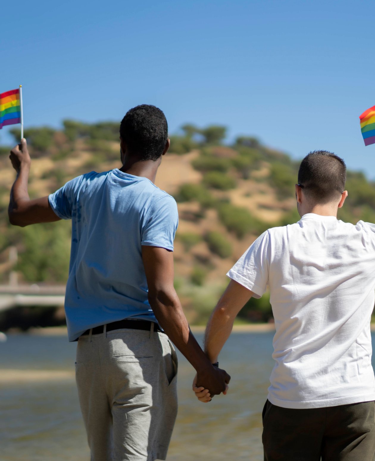 Zwei Männer halten sich an der Hand und schwenken Regenbogenfähnchen