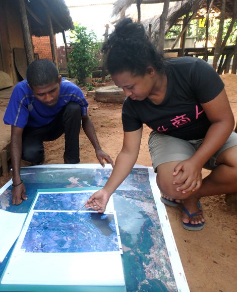 Eine Frau und ein Mann betrachten eine Landkarte. Afrikanische Hütten im Hintergrund.