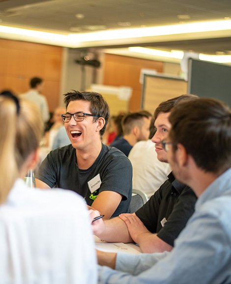 Bürger:innen an einem Tisch, ein Mann in der Mitte lacht