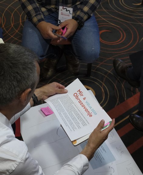 hen sitzen im Stuhlkreis und beugen sich über Arbeitspapiere und Notizzettel