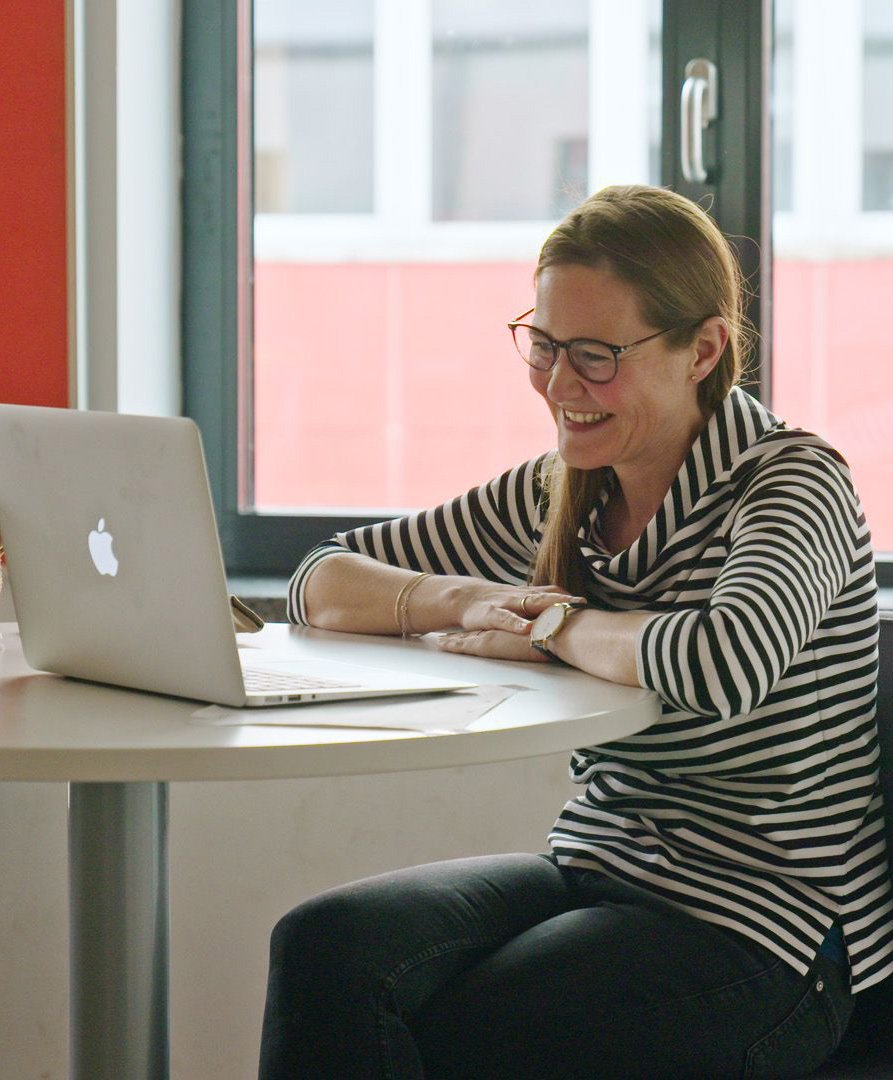 Eine Lehrerin sitzt an einem Tisch und schaut auf ihren Laptop