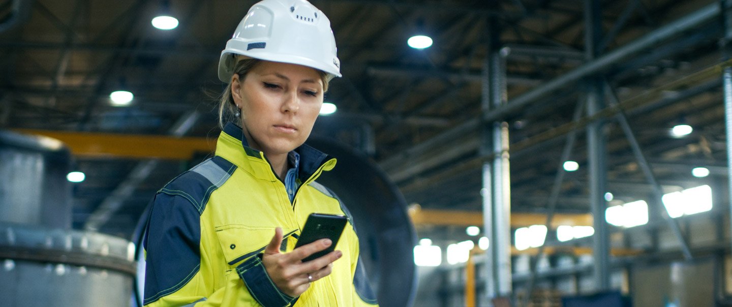 A woman in work clothes looks at her smartphone.