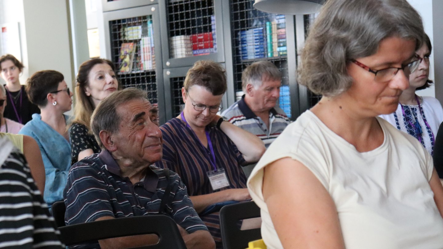 Menschen sitzen vor einer Wand mit vollen Bücherregalen