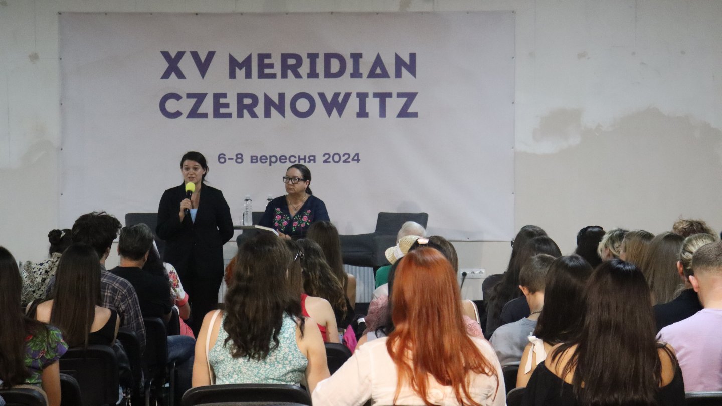 Publikum schaut auf ein Podium, auf dem mehrere Menschen sitzen