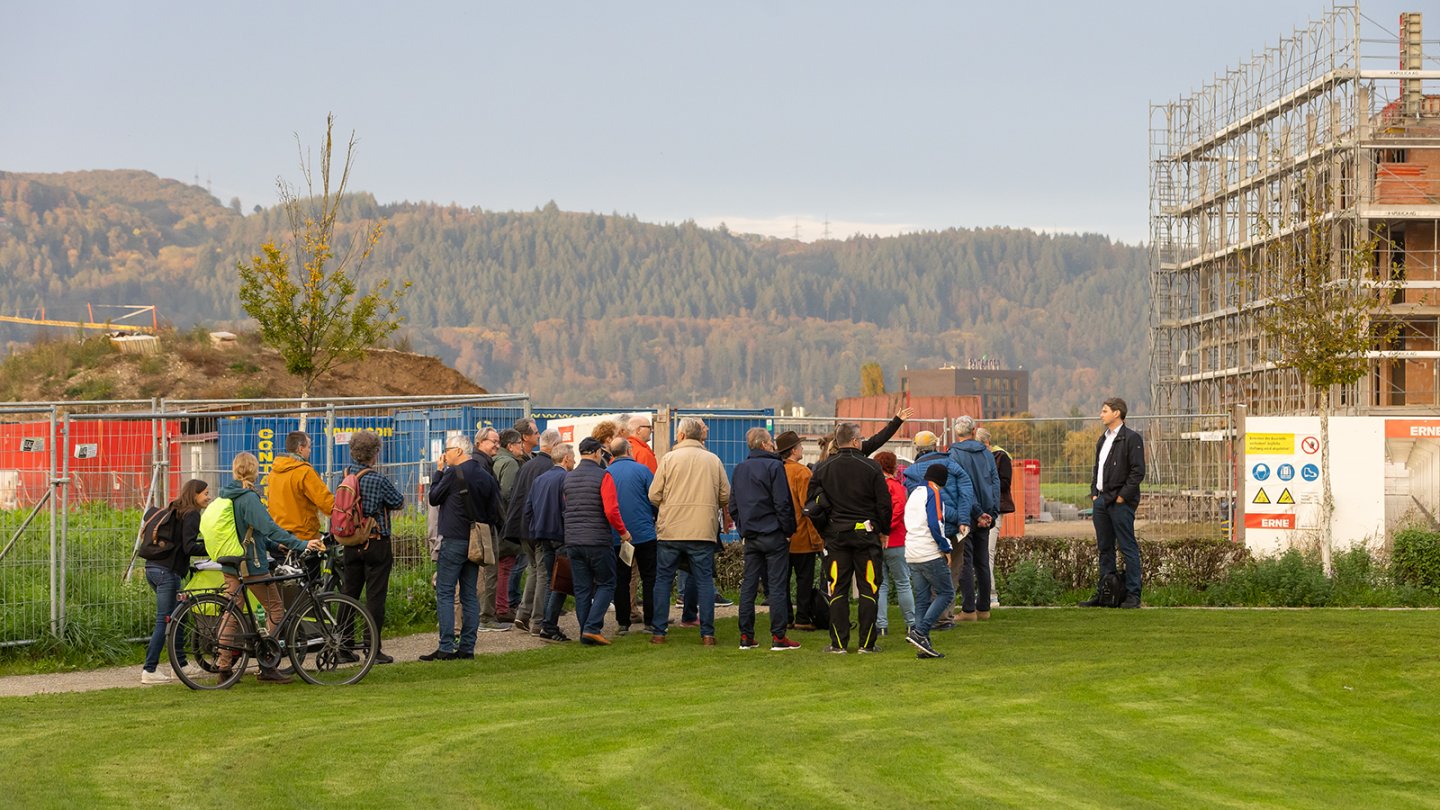 People are standing on a green meadow next to a construction site.