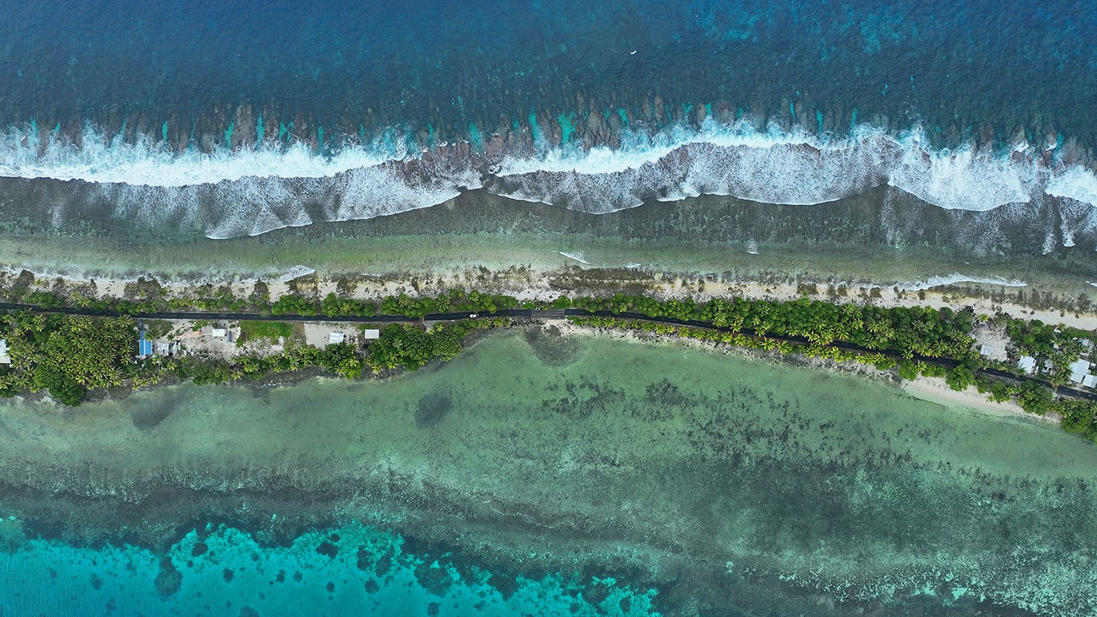 Road and houses on a narrow strip of land on the island of Tuvalu, surrounded by the sea and taken from the air.