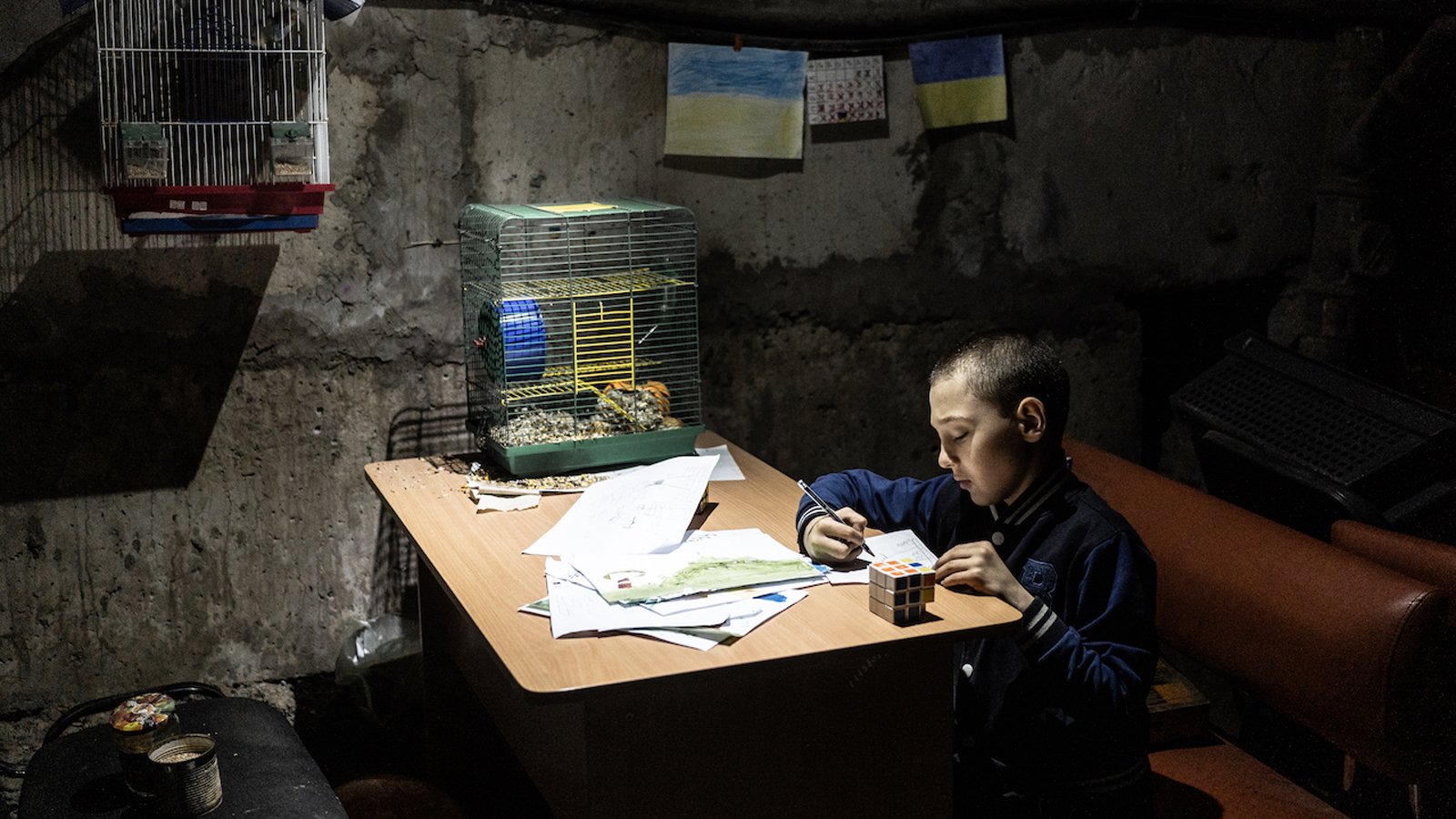 A boy is painting in the basement of a kindergarten. The walls are bare and the room is dimly lit.