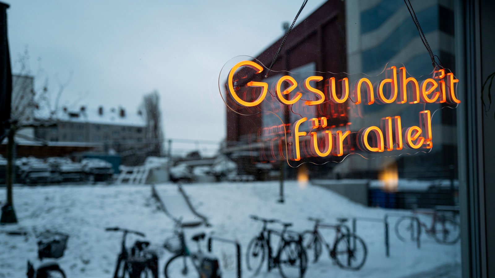 Blick durch ein Fenster in einen Hinnenhof mit einen leuchtenden Schrift "Gesundheit für alle!"