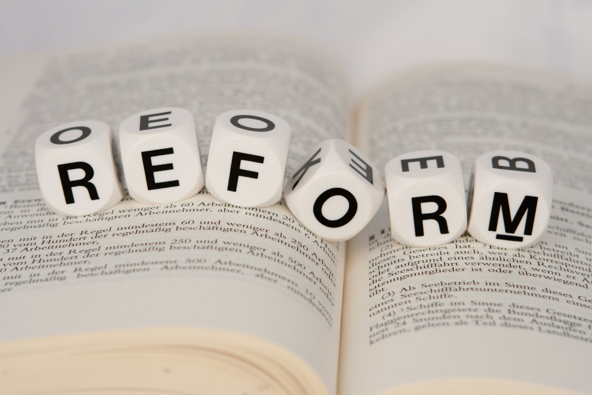 ünf weiße Würfel zeigen das Wort Reform und liegen auf einem aufgeschlagenen Gesetzesbuch
