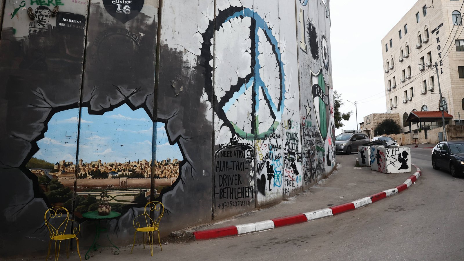 A view of the Israeli West Bank Barrier in Bethlehem. Next to a drawn peace symbol a painted hole in the wall is seen with two chairs and little table in front.