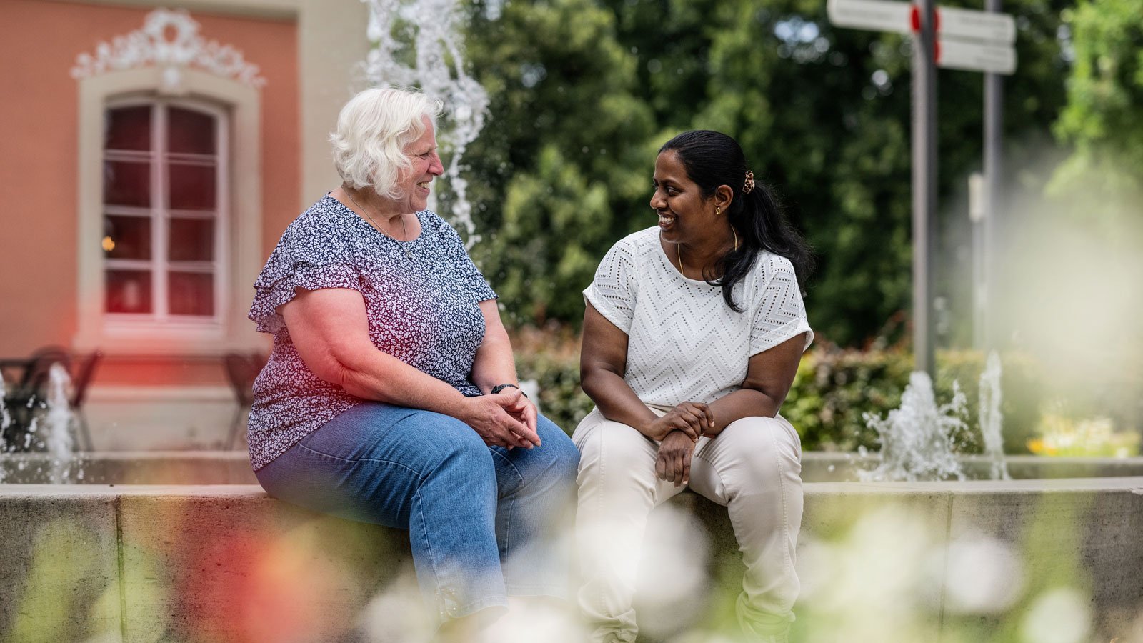 eine Seniorin und eine Altenpflegerin sitzen auf einer Parkbank