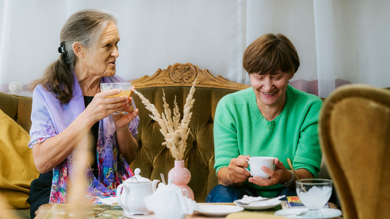 two women sit on a couch and drink tea