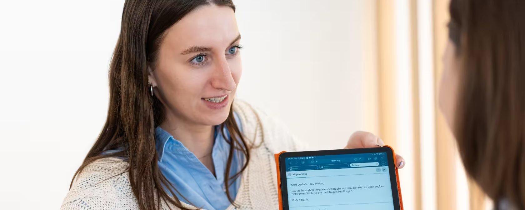 Eine junge Frau spricht mit einer weiteren Frau, die ein Tablet in der Hand hält