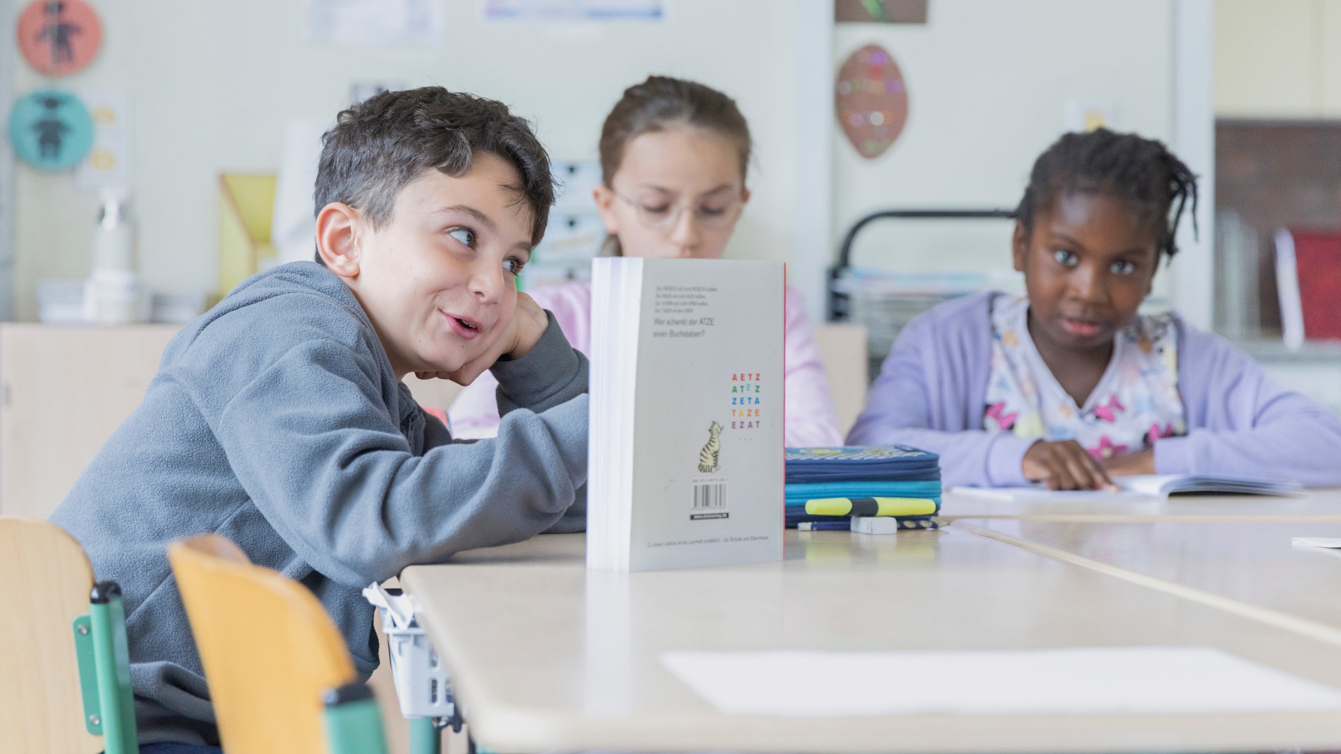 Drei Grundschulkinder sitzen an einem Tisch und lesen.