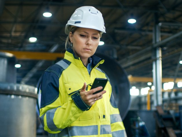 A woman in work clothes looks at her smartphone.