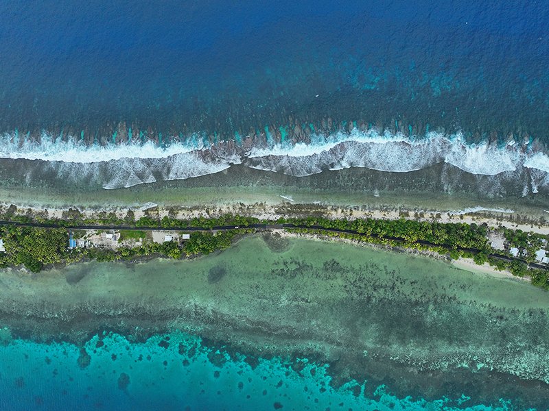 Straße und Häuser auf einem schmalen Landstreifen auf der Insel Tuvalu, umgeben vom Meer und aus der Luft aufgenommen.