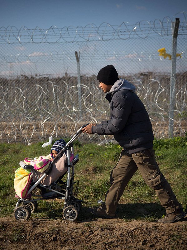 A man pushing a stroller in front of a border fence.
